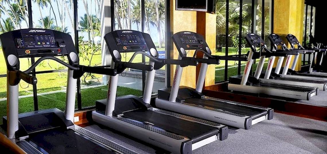 Fitnessstudio im Blue Water Hotel mit mehreren Laufbändern vor großen Fenstern.