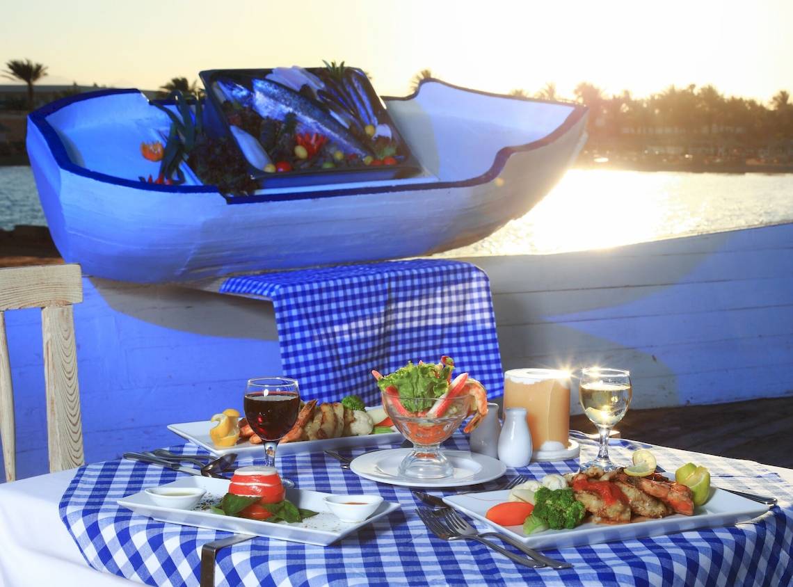 Ein Tisch im Restaurant des LABRANDA Club Makadi mit verschiedenen Gerichten und Getränken, darunter ein Fischboot im Hintergrund.
