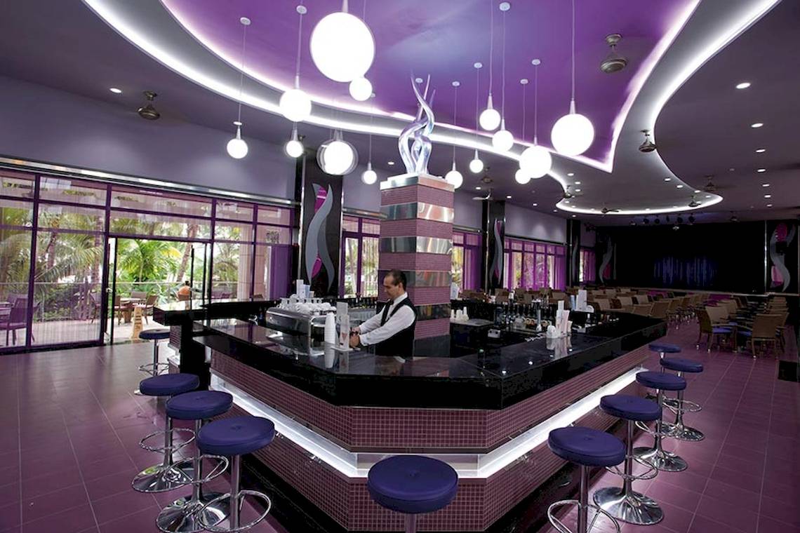Bar im Riu Caribe Hotel mit lila Einrichtung und blauen Stühlen.