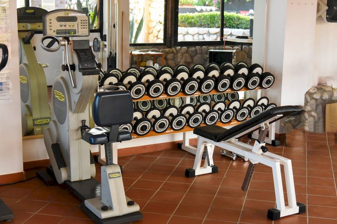 Fitnessstudio im Hotel Baia del Sole mit diversen Geräten und Hanteln.