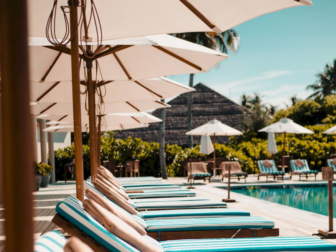 Pool-Lounge-Sessel unter Sonnenschirmen im Reethi Faru Resort