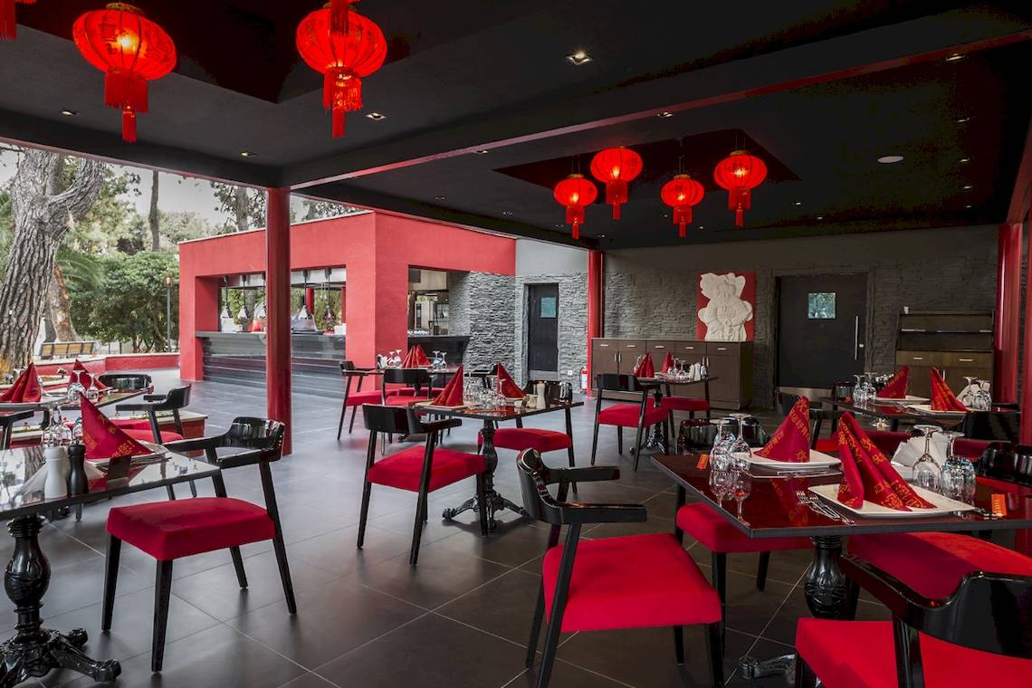 Innenbereich des Voyage Sorgun Restaurants mit roten Stühlen und Tischen, chinesischen Laternen und einer offenen Aussicht auf den Außenbereich.