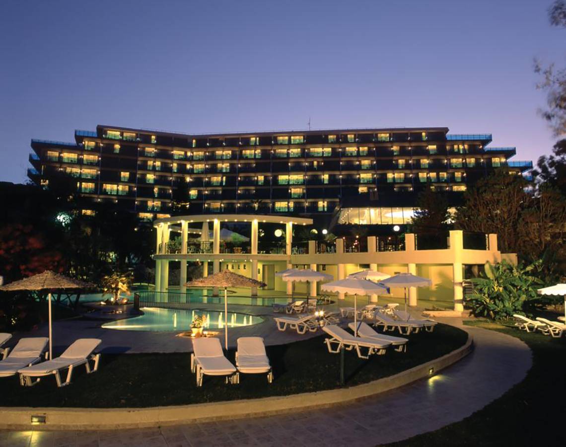Abendliche Ansicht des Calypso Beach Hotels mit illuminierten Fenstern und Außenbereich mit Pool und Liegestühlen.