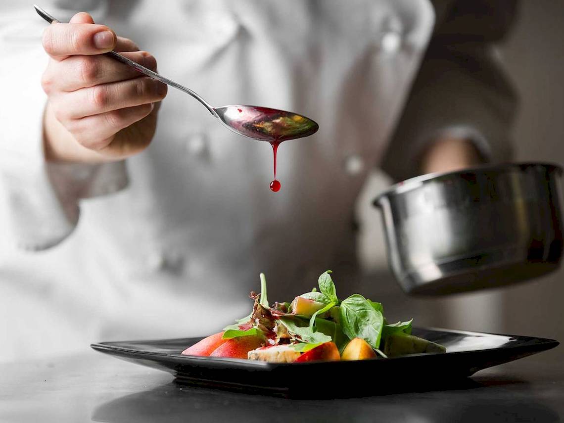 Koch tropft rote Sauce auf ein Salatgericht auf einem schwarzen Teller