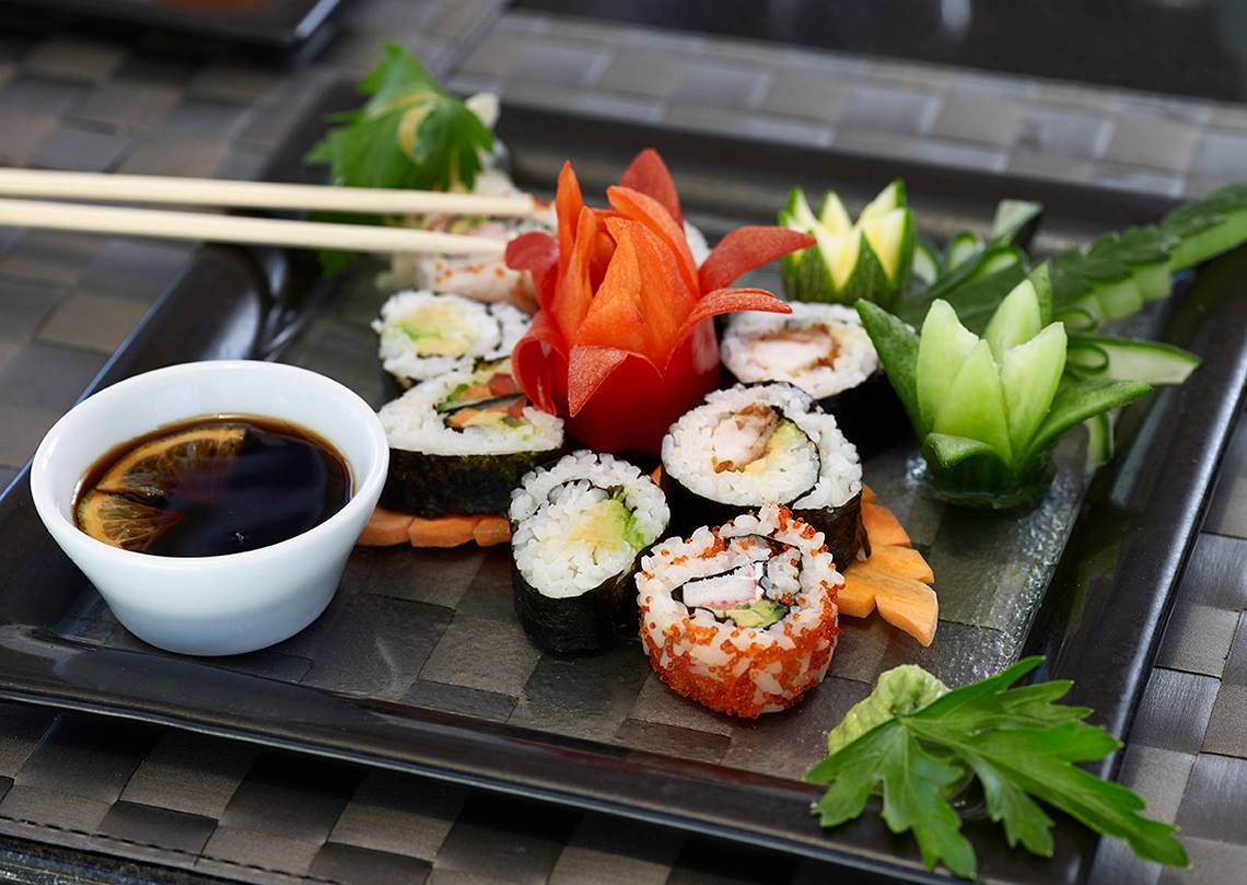 Ein Teller mit verschiedenen Sushi-Rollen, Sojasauce und Deko-Gemüse.