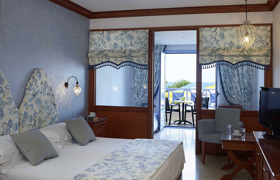 Innenansicht eines Zimmers im Serita Beach Hotel mit Blick auf einen Balkon und Meer.