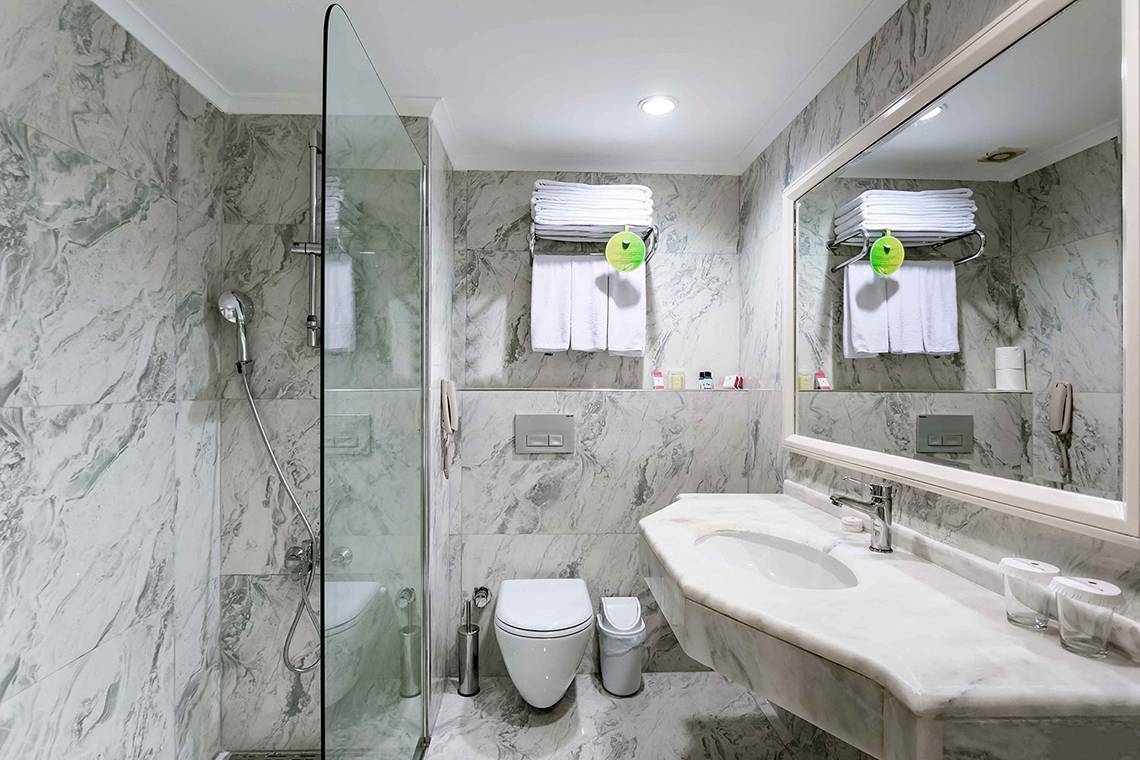 Badezimmer im Asteria Family Resort Side mit Marmorwänden, Duschkabine und Waschbecken.