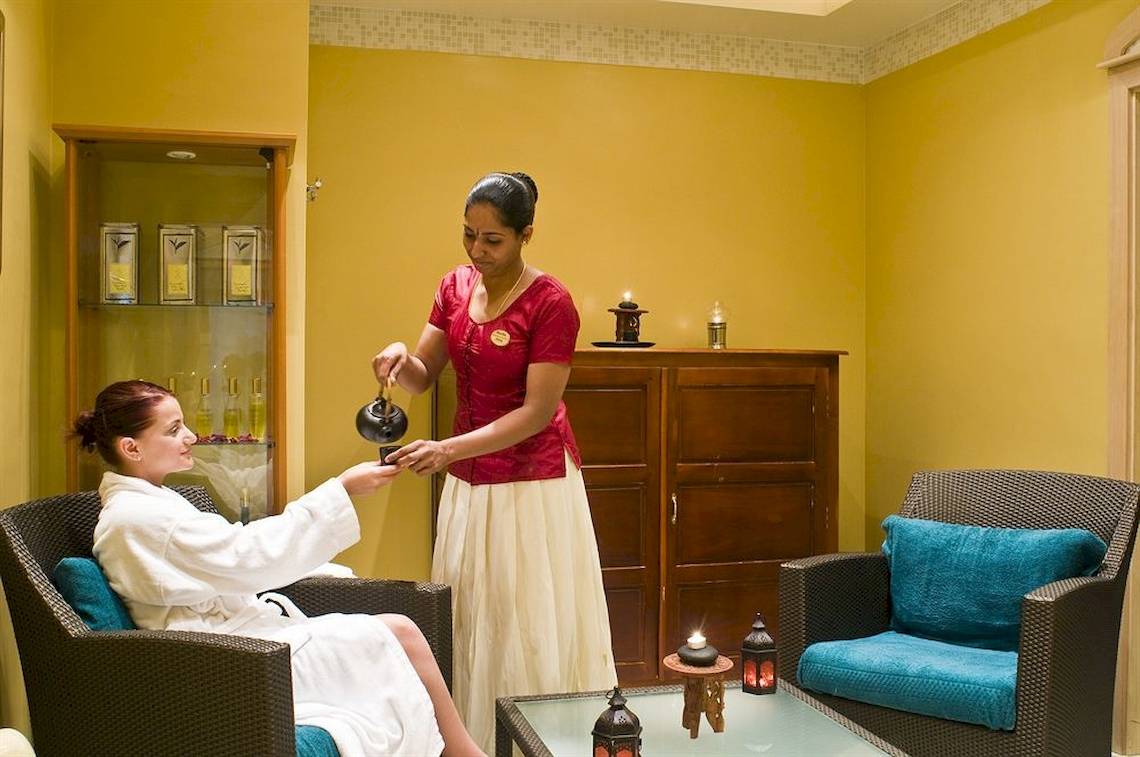 Frau im Bademantel bekommt Tee von einer Bediensteten im Radisson Blu Resort & Spa, Malta Golden Sands
