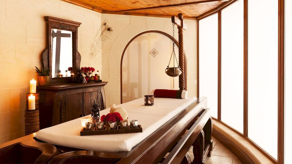 Spa-Behandlungsraum im Kempinski Hotel San Lawrenz Malta mit einem Massagetisch, Kerzen und einem Spiegel.