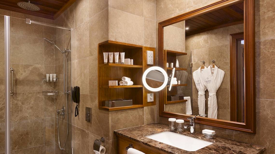 Badezimmer im Kempinski Hotel San Lawrenz Malta mit Regendusche, Spiegel und Waschbecken.