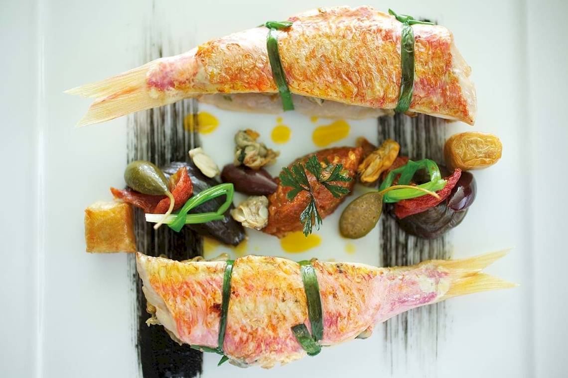 Zwei gebratene Fische mit Gemüse auf einer weißen Platte serviert.