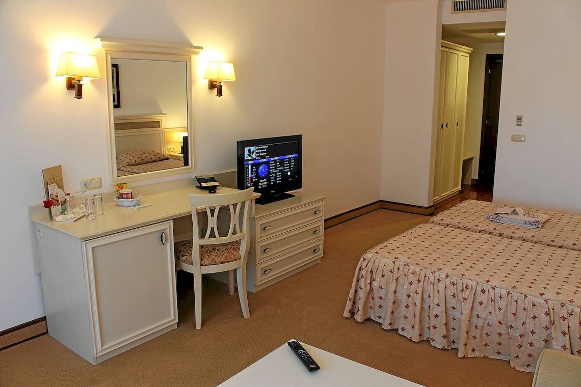 Hotelzimmer im Helena Sands Hotel mit Schreibtisch, Stuhl, Fernseher und zwei Betten.