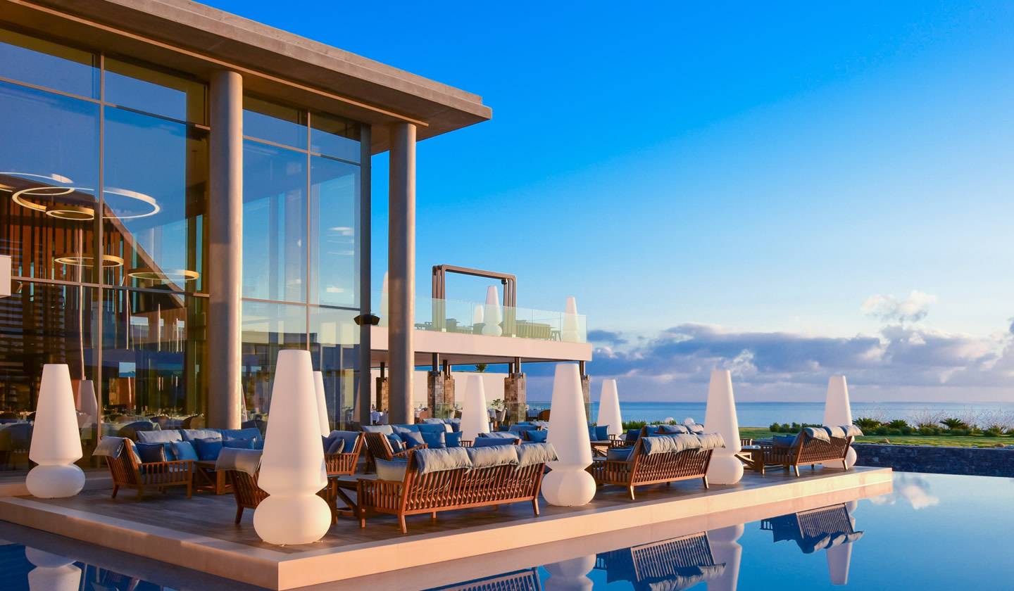 Außenbereich des Nana Princess Suites, Villas & Spa Hotels mit Swimmingpool und Blick auf den Ozean bei Sonnenuntergang.