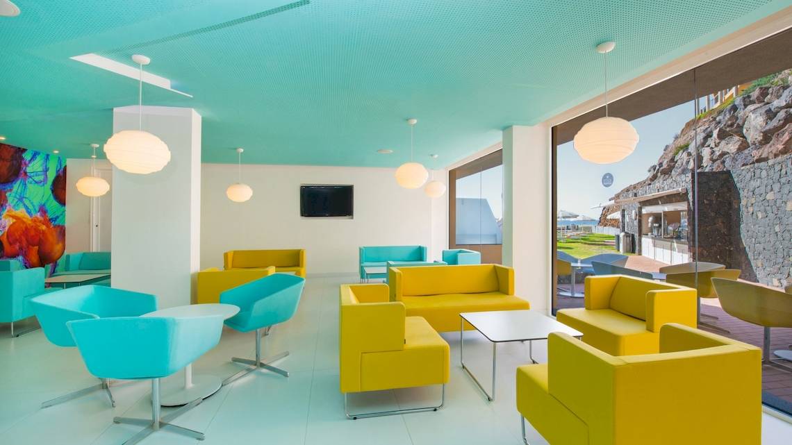 Innenansicht des Hotellobbys im Iberostar Playa Gaviotas Park mit blauen und gelben Möbeln und einer großen Fensterfront.