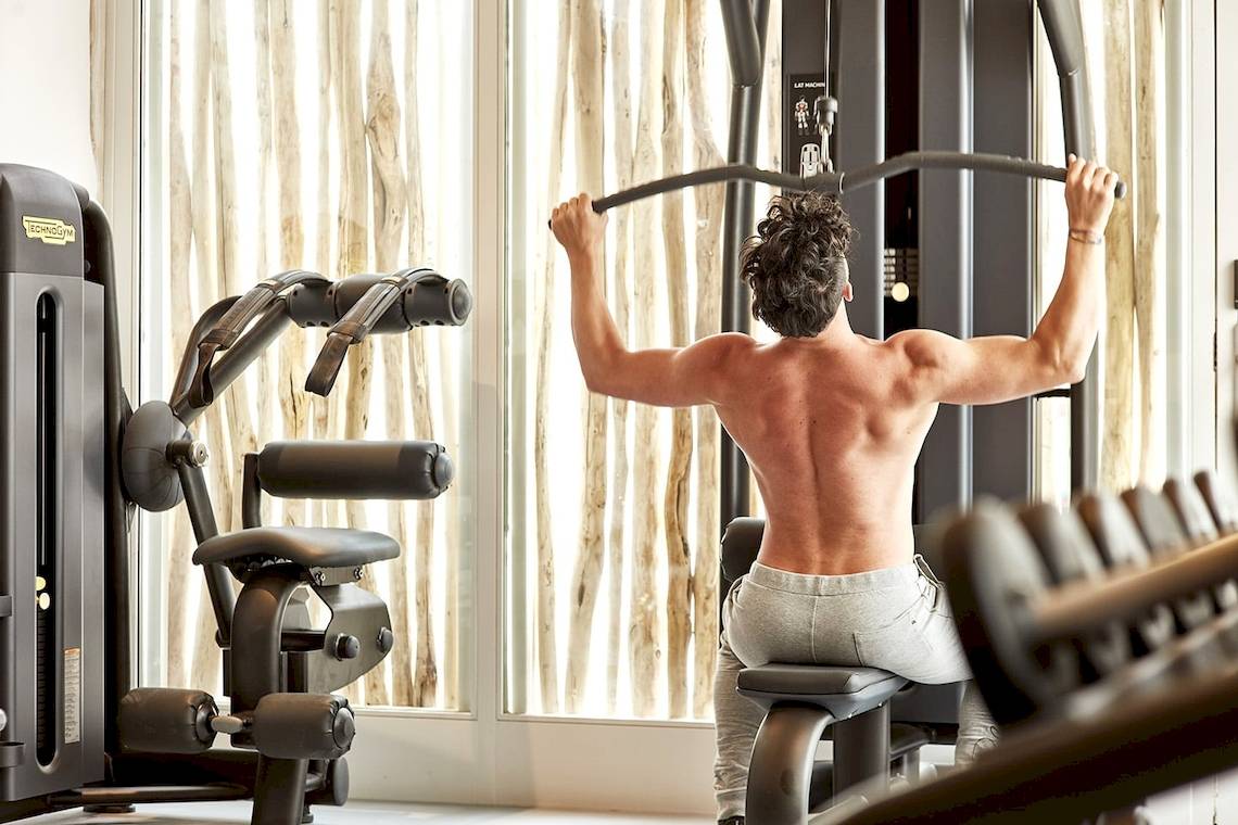 Mann im Fitnessbereich des Mykonos Ammos Hotels, der eine Lat-Maschine benutzt.