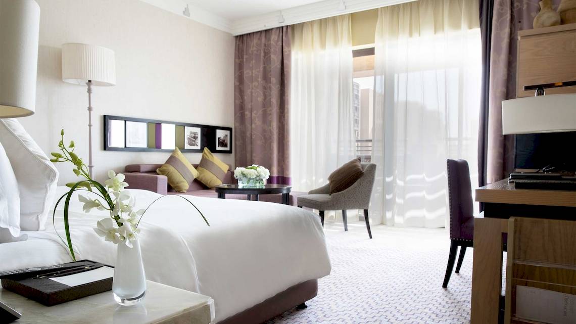 Innenansicht eines Hotelzimmers im Jumeirah Mina A'Salam mit Bett, Tisch, Stuhl und Fenstern.