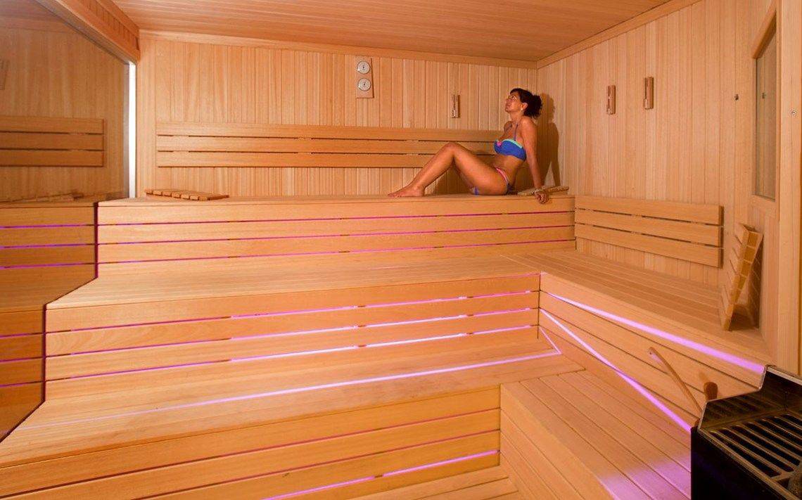 Frau sitzt in einem Holzsauna mit blauen und rosa Lichtern