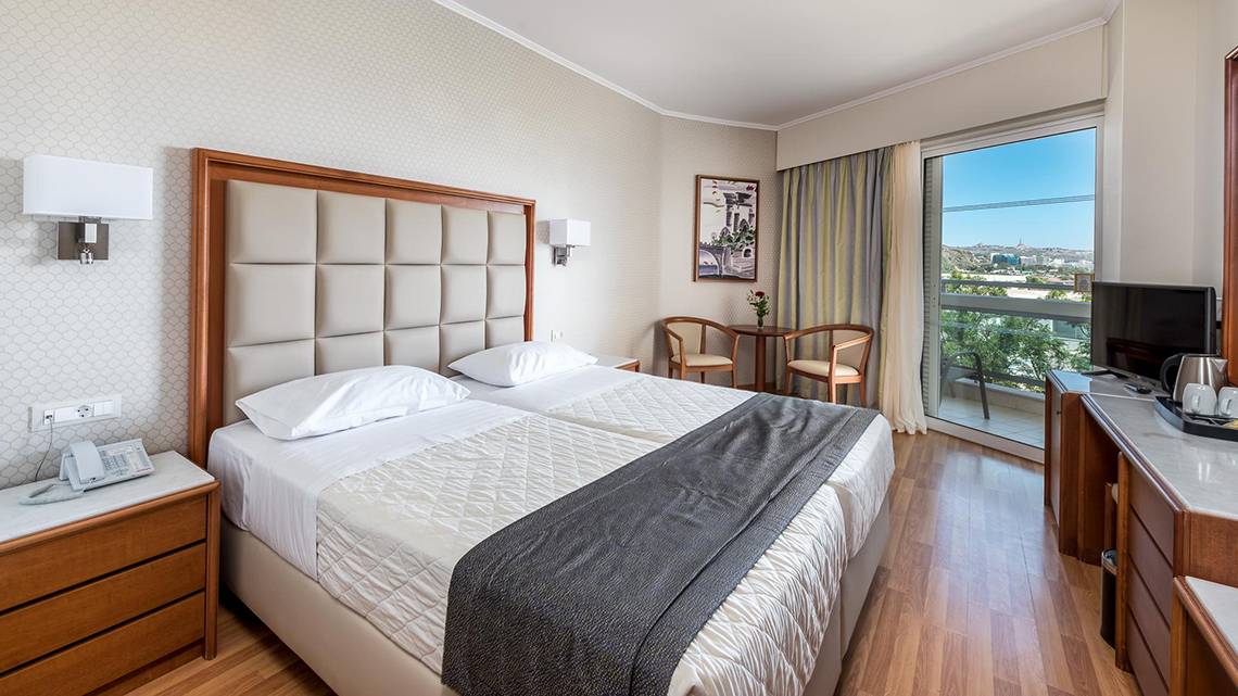 Doppelzimmer im Apollo Beach Hotel mit zwei Betten, Nachttischen und einer Aussicht auf die Stadt.