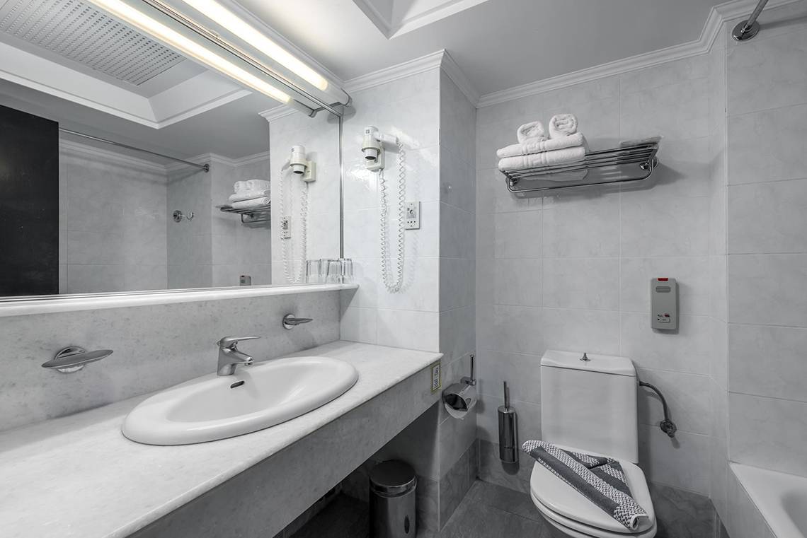Badezimmer im Apollo Beach Hotel mit Waschbecken, Spiegel, Toilette und Handtüchern.