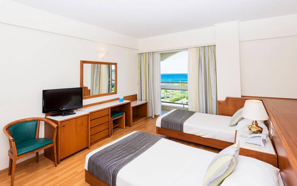Doppelzimmer mit Meerblick im Apollo Beach Hotel mit zwei Betten, Fernseher, Schreibtisch und Balkon.