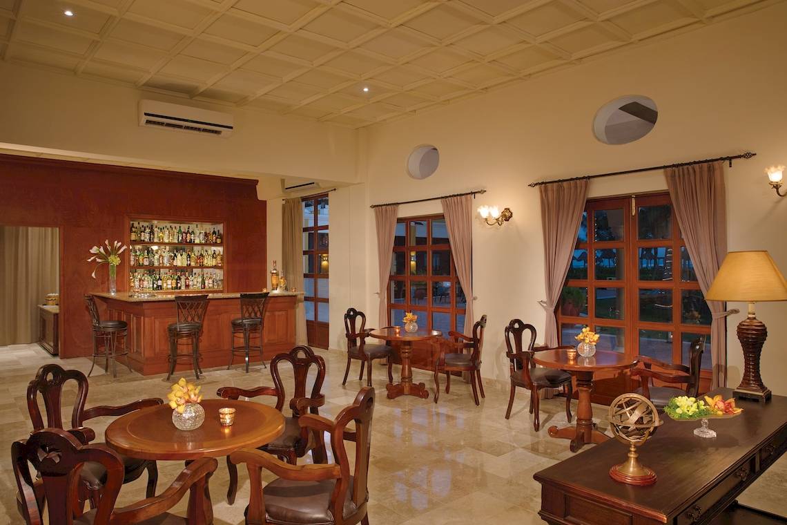 Lobby Bar Bereich im Dreams Tulum Resort & Spa mit Holztischen, Stühlen und einer Bar.