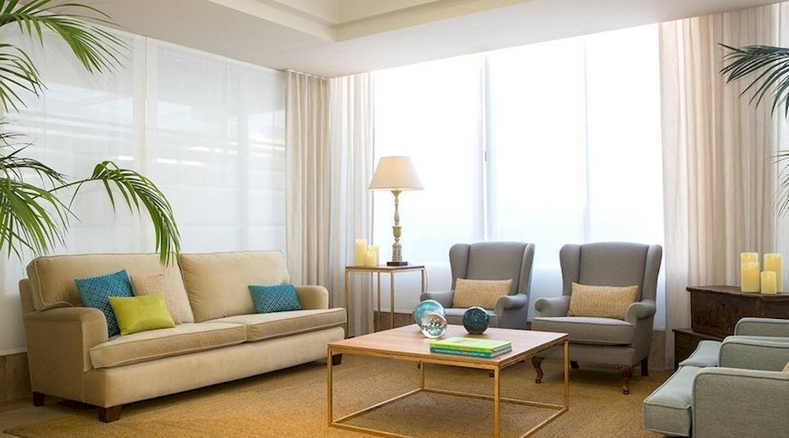 Wohnzimmer im Universal Hotel Neptuno mit Sofa, Sesseln, Tisch und Lampe.