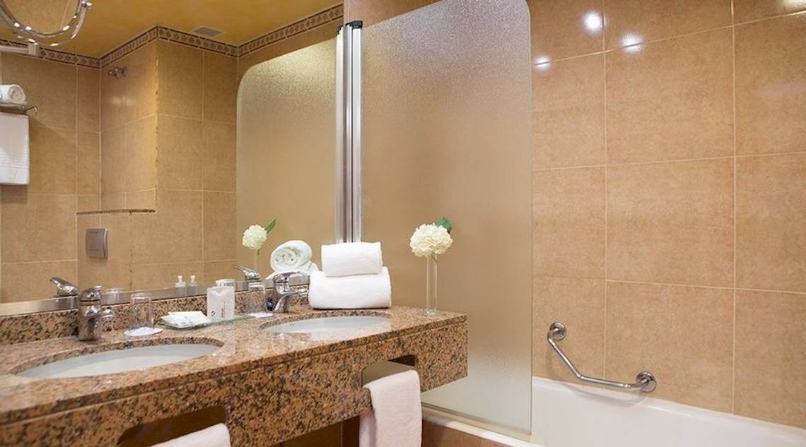 Badezimmer im Universal Hotel Neptuno mit zwei Waschbecken, Spiegel, Badewanne und Handtüchern.