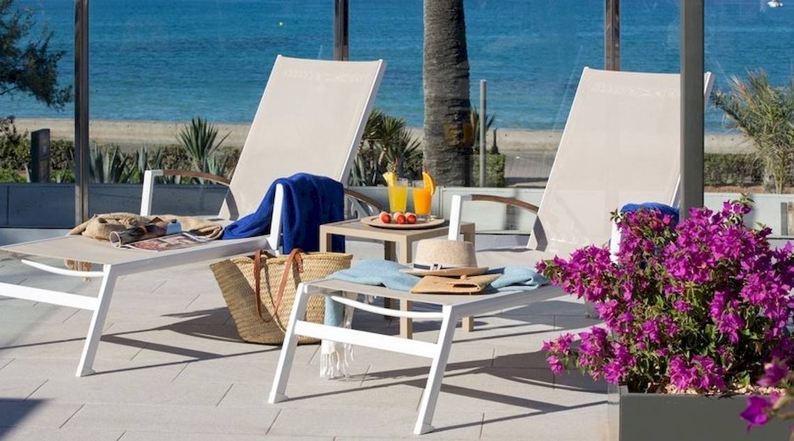 Zwei weiße Liegen auf der Terrasse des Universal Hotel Neptuno mit Meerblick, Getränken und Blumen.