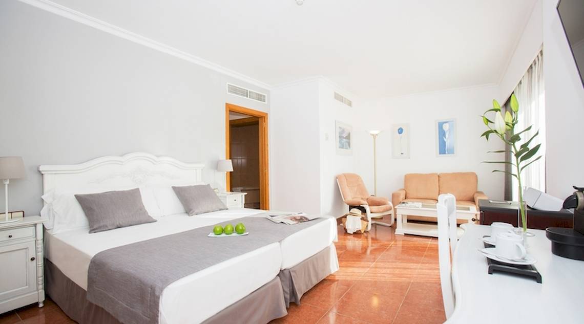 Doppelzimmer im Universal Hotel Neptuno mit zwei Betten, einem Wohnzimmerbereich, einem Couch, einem Tisch und einem Blumentopf.