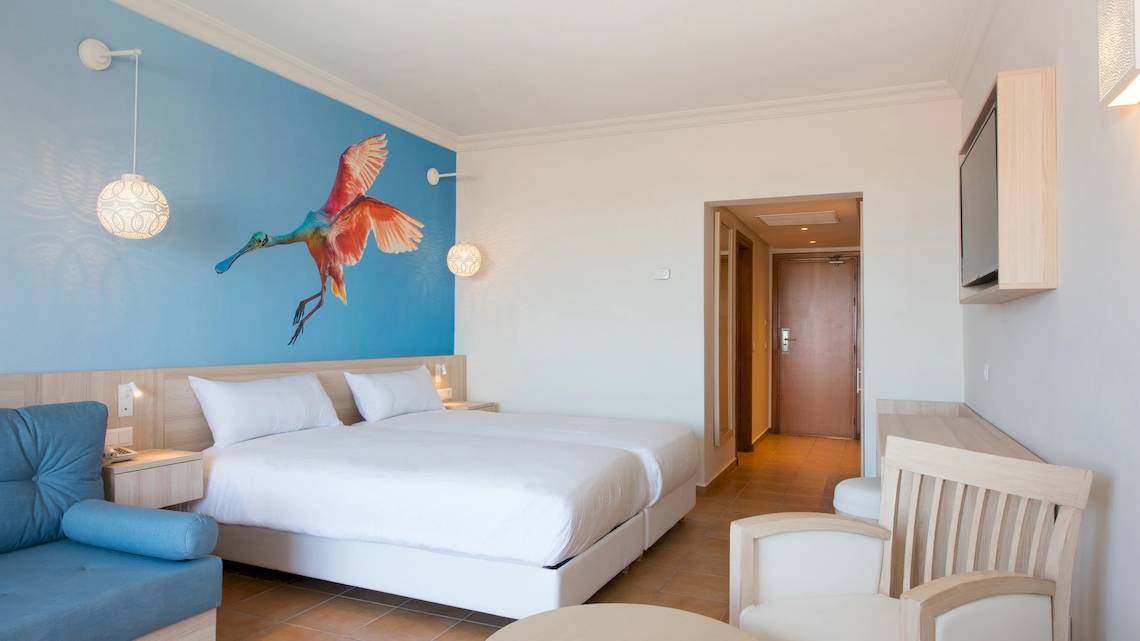 Doppelzimmer im Iberostar Founty Beach Hotel mit zwei Betten, blauer Wand und Vogelmalerei.