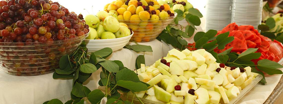 Ein Obstbuffet auf einem Tisch mit verschiedenen Früchten wie Trauben, Äpfeln, Aprikosen und Melonen, dekoriert mit grünen Blättern.