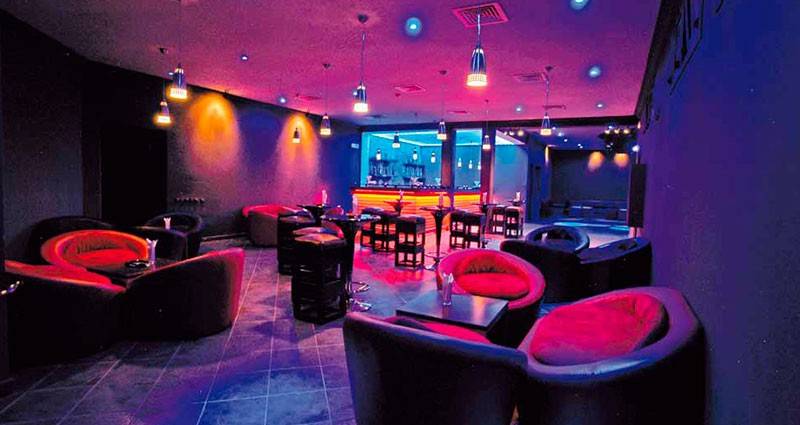 Bar-Lounge im Royal Decameron Issil Resort mit rot-schwarzer Inneneinrichtung und violetten Lichtern.