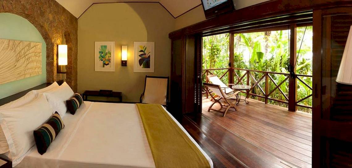 Innenansicht eines Hotelzimmers im Paradise Sun Hotel mit einem großen Bett, einem Balkon und einer Aussicht auf den Dschungel.