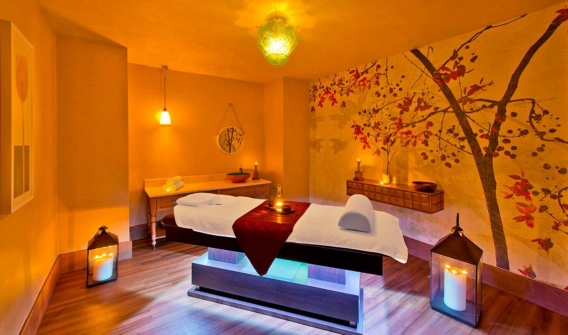 Massage-Behandlungsraum im Titanic Deluxe Lara Hotel mit einem Therapiebett, Kerzen und dekorativen Elementen.