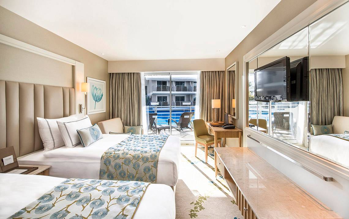 Ein Hotelzimmer des Titanic Deluxe Lara mit zwei Betten und Blick auf einen Pool.