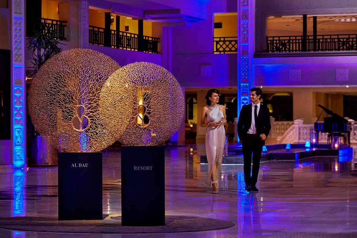 Paar vor dem Steigenberger ALDAU Beach Resort beim Eingang mit zwei goldenen Kunstwerken.