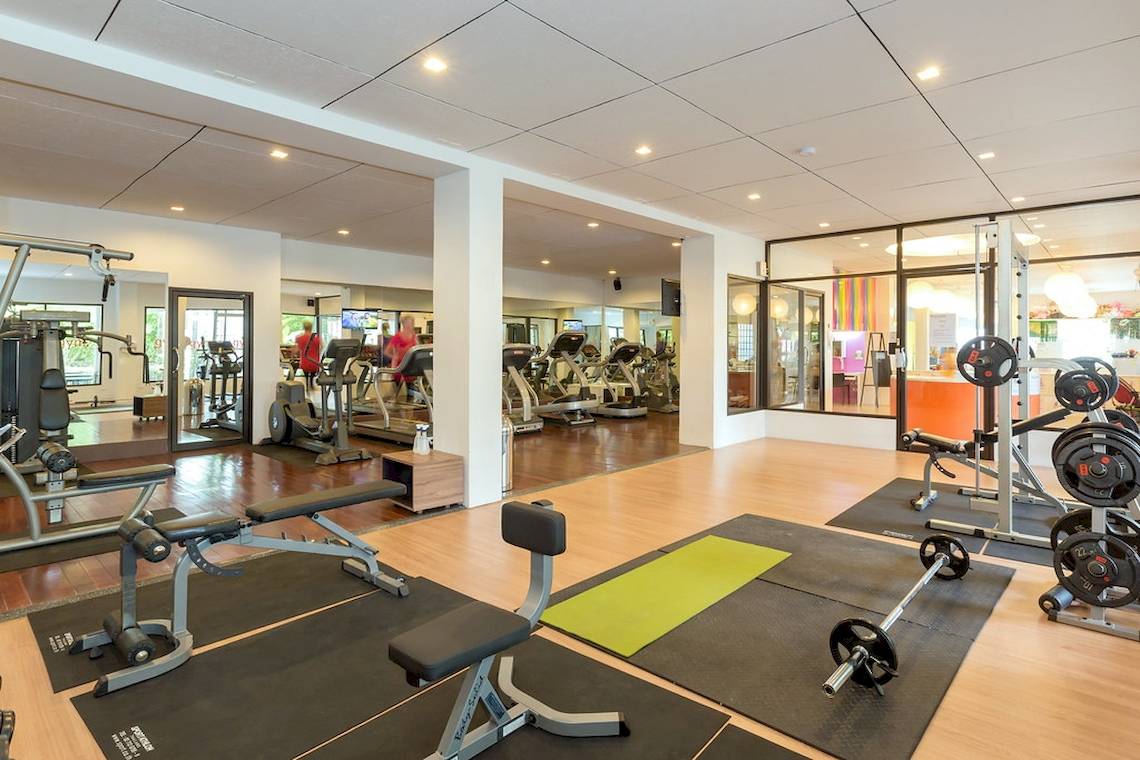 Fitnessstudio im Sunwing Kamala Beach Hotel mit verschiedenen Trainingsgeräten und einer Person, die Cardiogeräte benutzt.