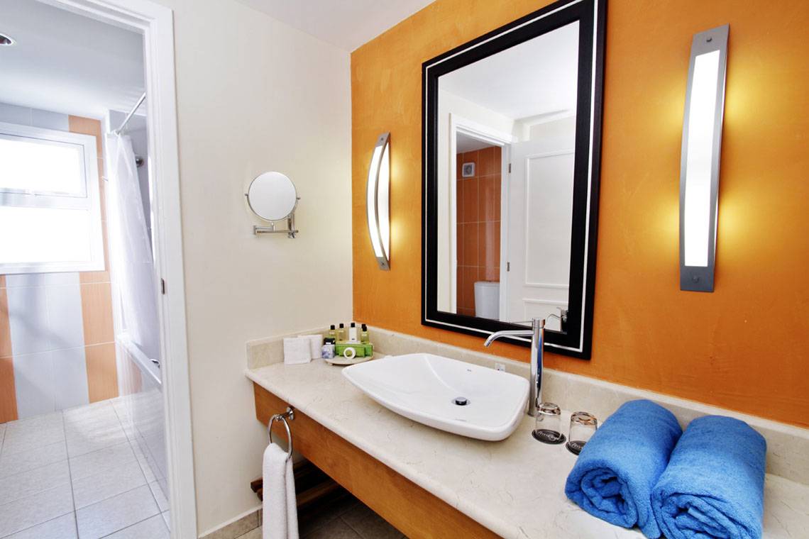 Badezimmer im Valentin Varadero El Patriarca Hotel mit Waschbecken, Spiegel und blauen Handtüchern.