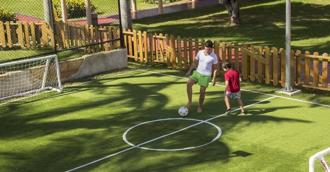 Mann und Kind spielen Fußball auf einem Fußballfeld im Grand Palladium Bavaro Suites Resort & Spa.