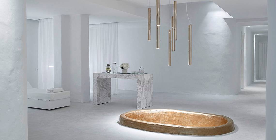 Innenansicht des Knossos Beach Bungalows Suites Resort & Spa mit ovaler Badewanne, Tisch und Lampen.