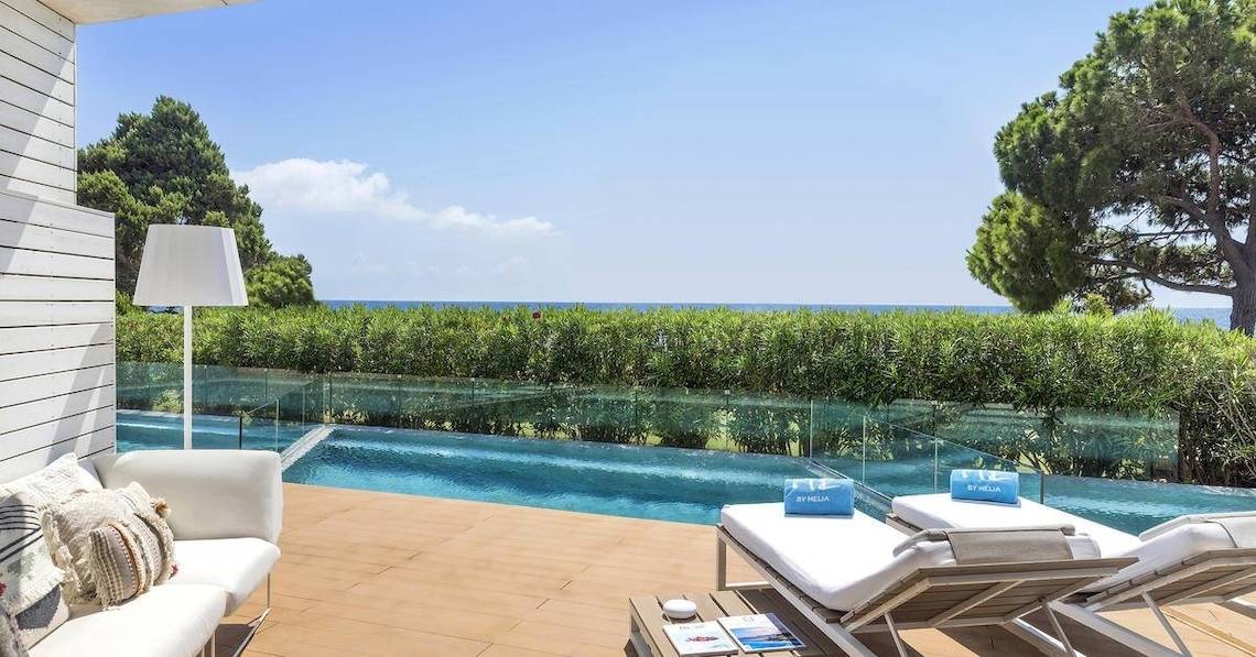 Außenbereich des ME Ibiza Hotels mit Pool, Loungemöbeln und Blick auf das Meer.
