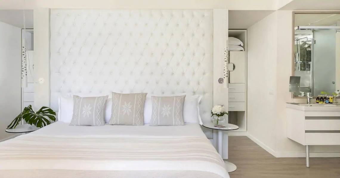 Schlafzimmer im ME Ibiza Hotel mit einem großen Bett, weißen Kissen und einem gepolsterten Kopfteil.
