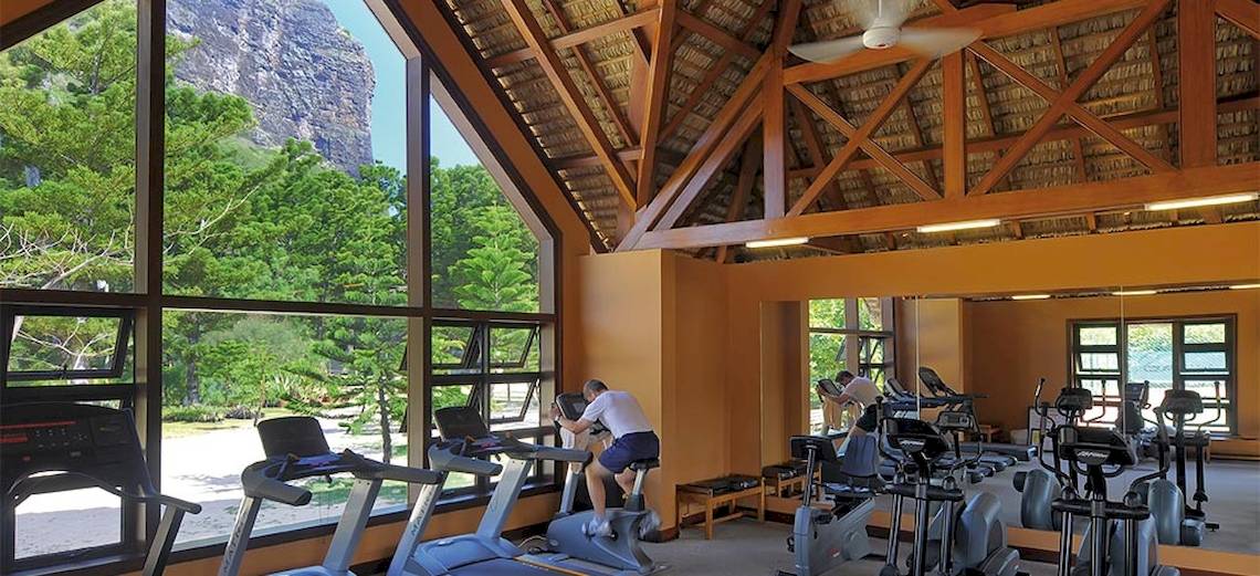 Fitnesscenter im Dinarobin Beachcomber Golf Resort & Spa mit großen Fenstern und Ausblick auf Berge