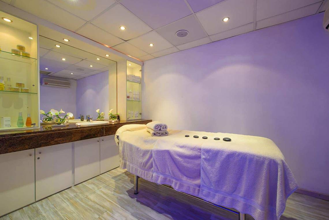 Spa-Behandlungsraum im Golden Bay Beach Hotel mit Massagetisch, Handtüchern und Aromatherapie-Steinen.