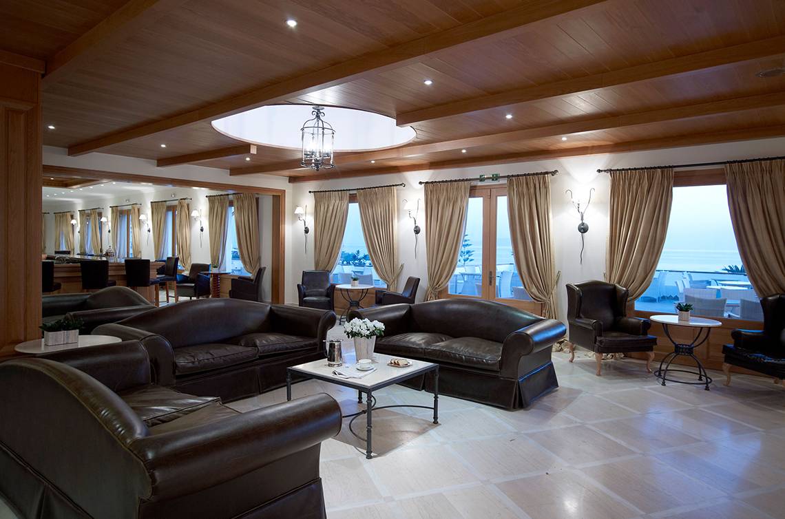Lobby-Lounge des Mitsis Rinela Beach Hotels mit braunen Ledersofas und großen Fenstern.