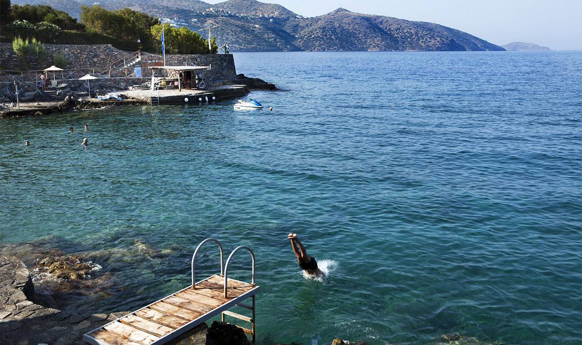 Person springt ins Meer am Minos Palace Hotel & Suites, umgeben von Klippen und Bergen.