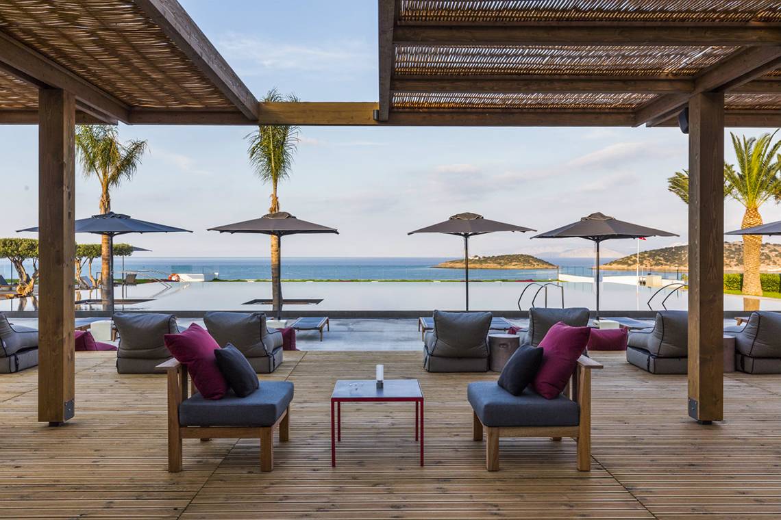 Außenbereich des Minos Palace Hotel & Suites mit Blick auf das Meer und Loungemöbeln.