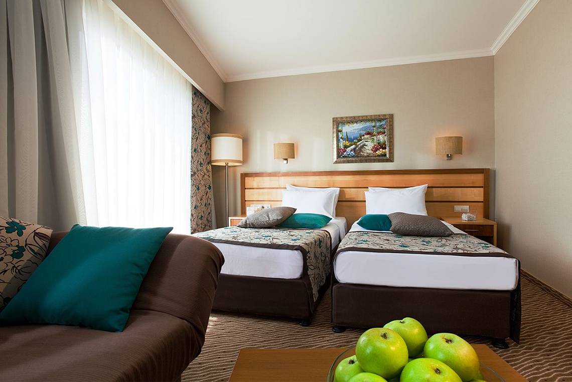 Doppelbettzimmer im Side Sun Hotel mit zwei Betten, Kissen, Couch und Obstschale.