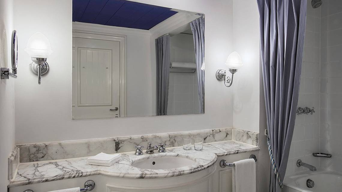 Ein Badezimmer mit weißem Marmor, Spiegel, Waschbecken, Badewanne, und Lampen.