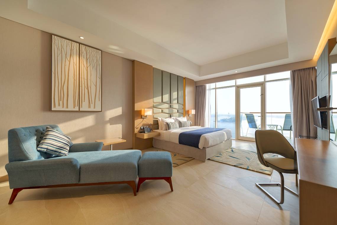 Innenansicht einer Suite im Royal Central Hotel The Palm mit Bett, Möbeln und Meerblick.
